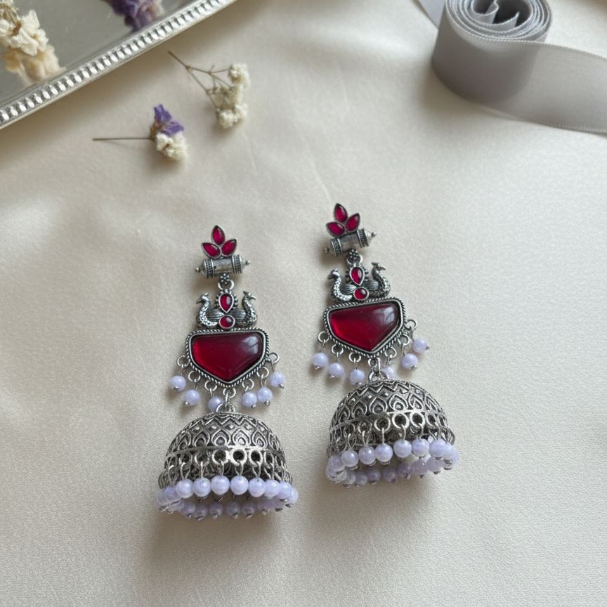 Ornate earrings with red stones and pearl-like beads on a light surface.