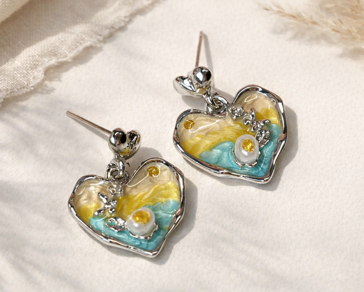 Heart-shaped earrings with yellow and blue design on a textured fabric background