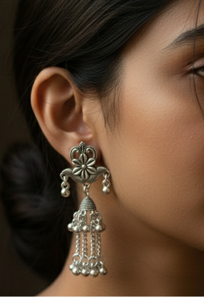 Silver earrings with floral design and dangling beads worn by a person.