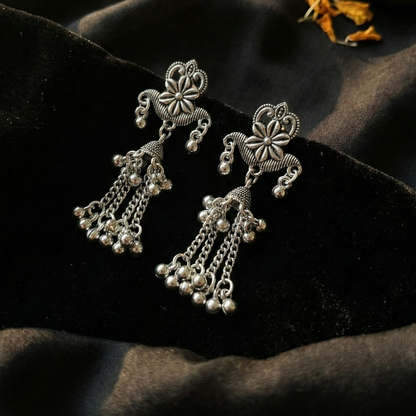 Silver earrings on a dark fabric background with a small pot and flowers.