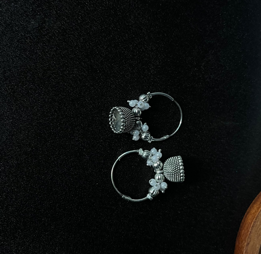 Pair of silver hoop earrings with floral designs on a black surface.