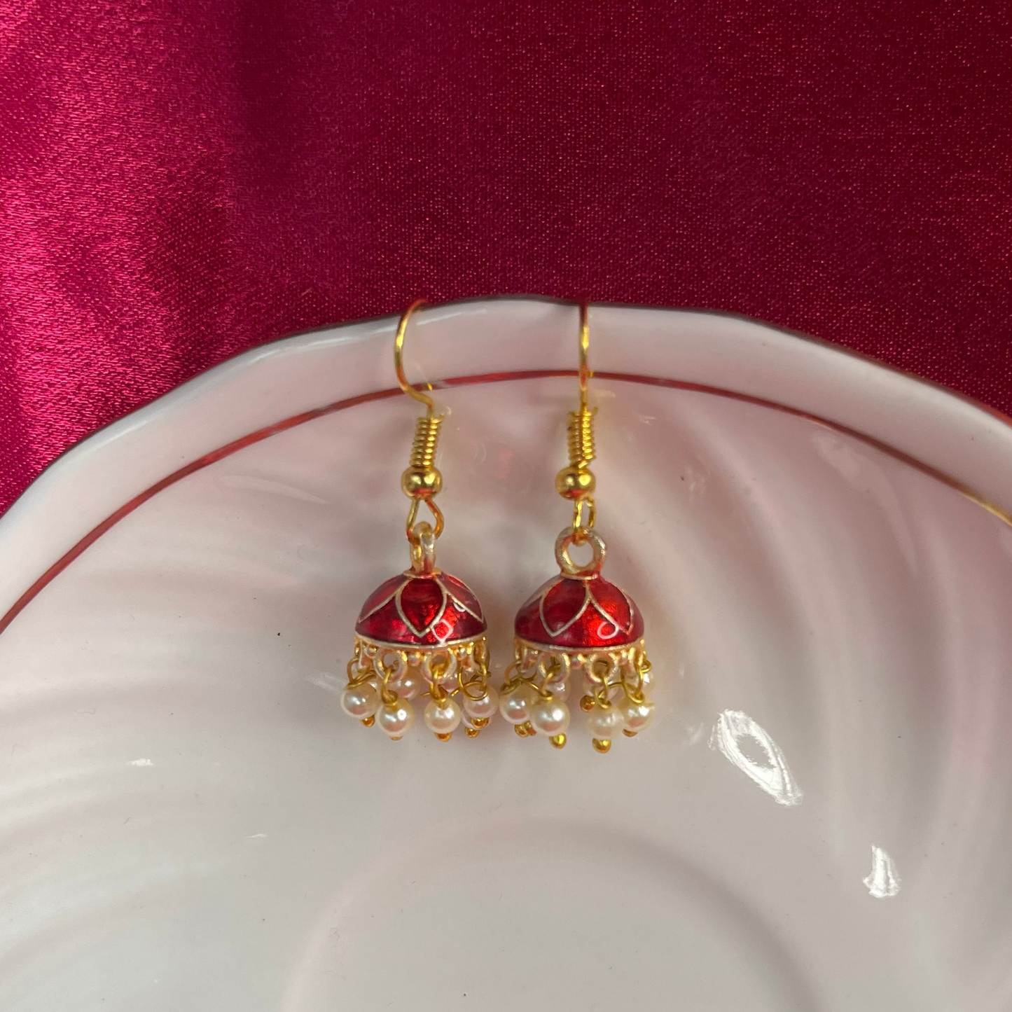 Red and gold earrings on a white dish with a red background