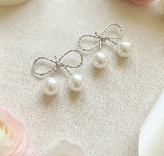 Pearl earrings with silver bows on a decorative surface with pink flowers and ribbons.