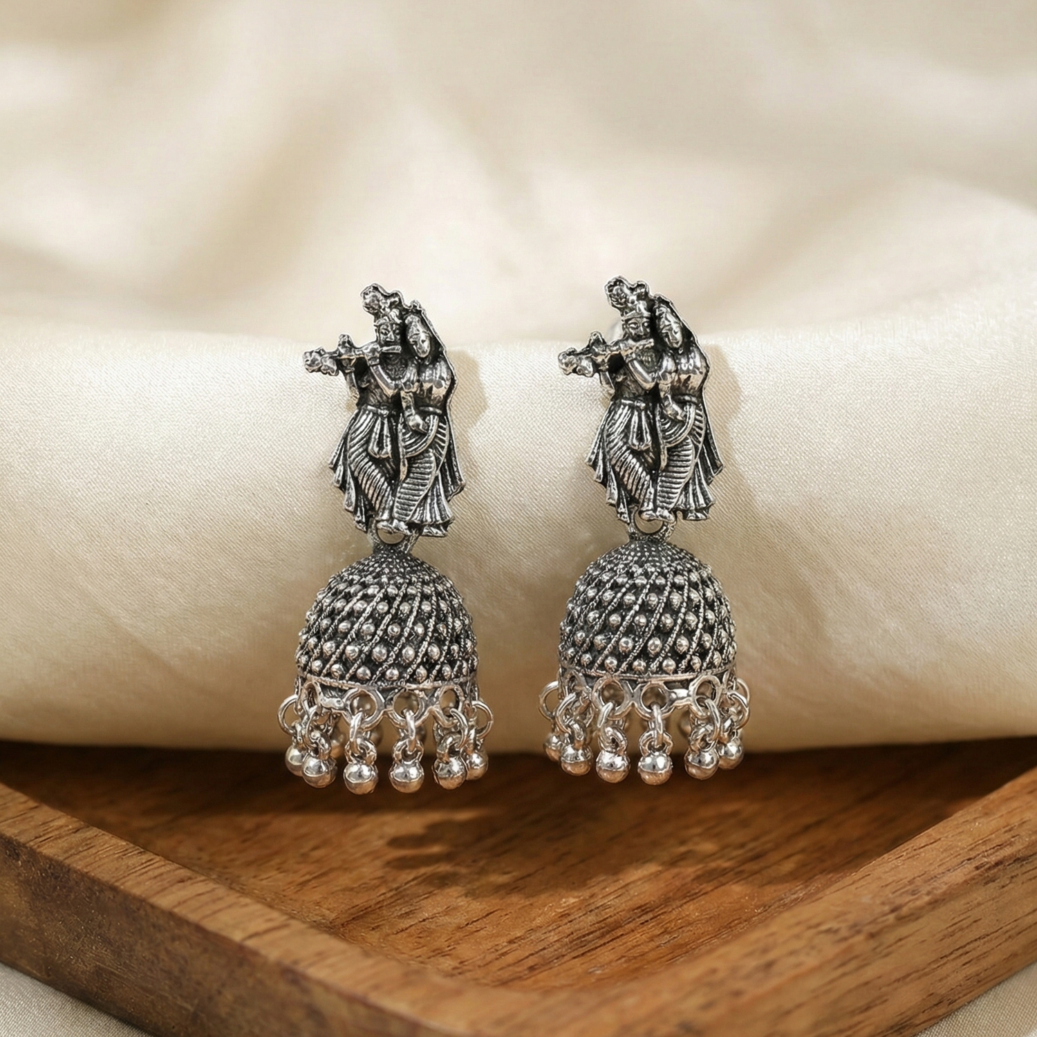 Pair of silver jhumka earrings on a wooden surface with a soft beige background