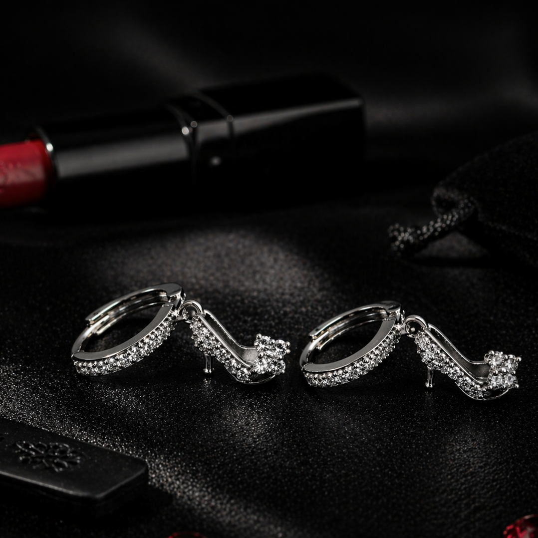 Silver high-heeled shoe earrings on a dark surface with red lipstick and gemstones.
