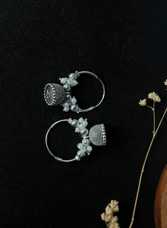 Silver floral earrings on a dark surface with dried flowers.
