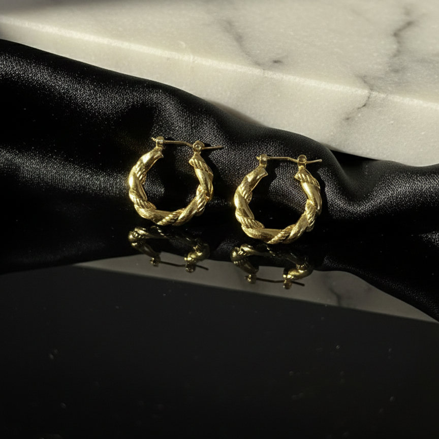 Gold hoop earrings on a black satin surface with a marble background